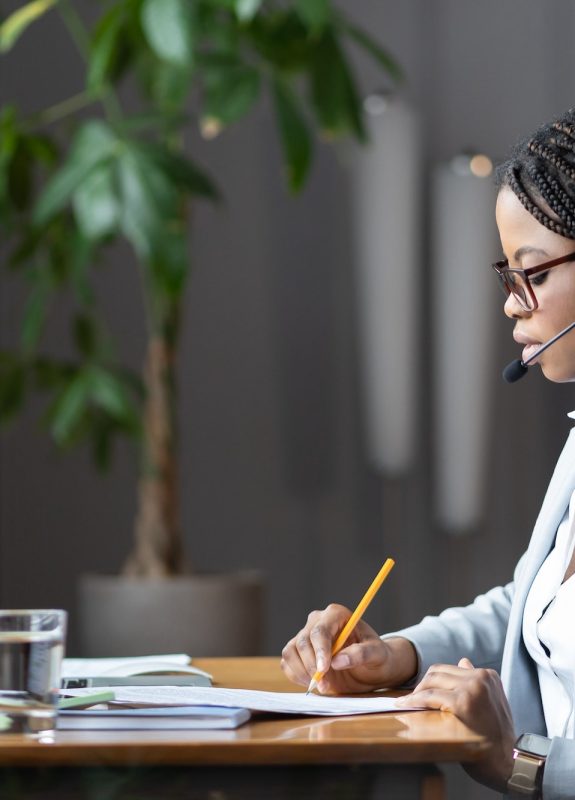 focused-african-female-home-based-virtual-assistant-in-headset-making-notes-during-online-meeting.jpg